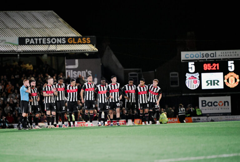 Grimsby Town FC Players arm in arm on the pitch against Manchester Utd